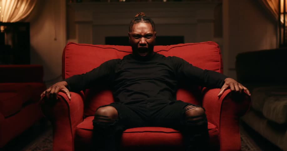Man sits in dimly lit room in red chair and screams