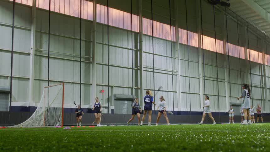 A female lacrosse team celebrates after scoring a goal against the other team on an indoor lacrosse field at sunset