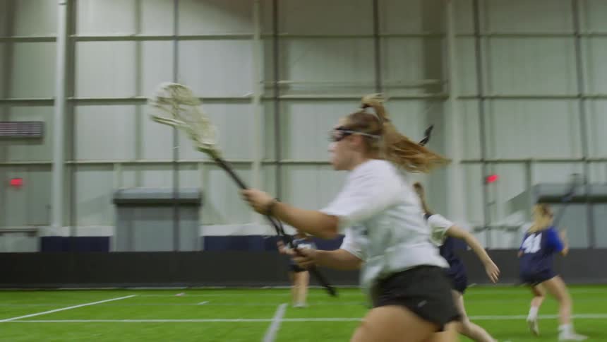 Women playing lacrosse in an indoor field