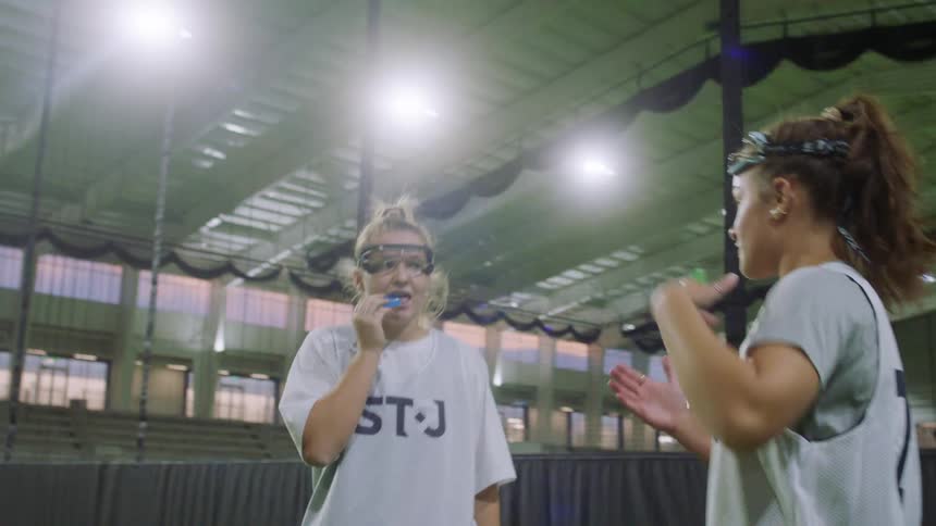 Two teenage girls give direction about an indoor lacroose game