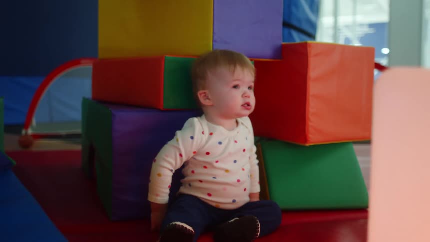 A baby trying to walk in a play area with large soft blocks falls down