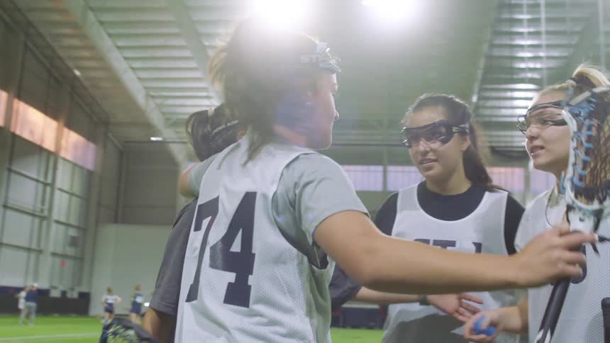 A high school female lacrosse team huddles together during an indoor match
