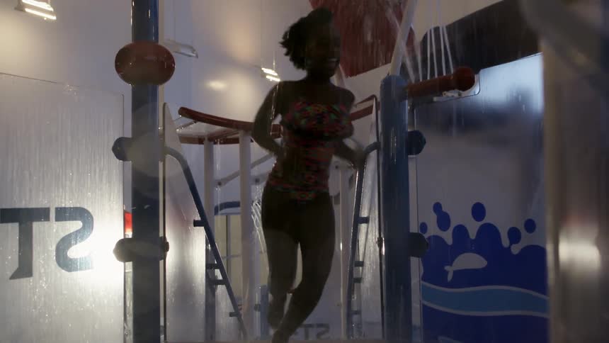 A young girl runs up stairs and through water spraying at an indoor pool
