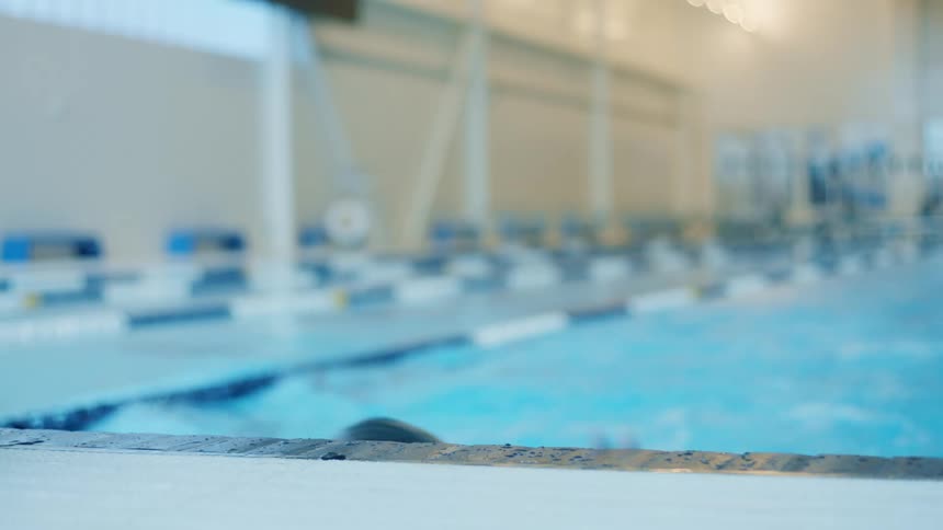 A man swims in the pool and stops to remove his goggles