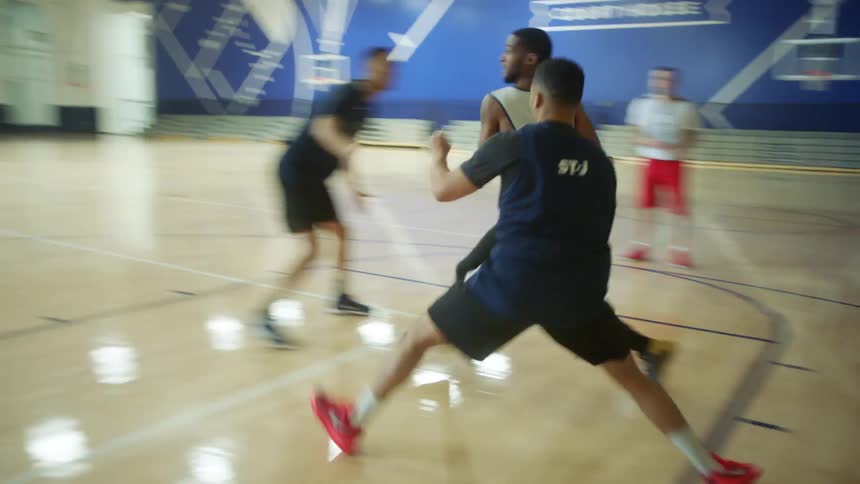 A teenage boy dribbles and shoots and makes a basket as four people play basketball together