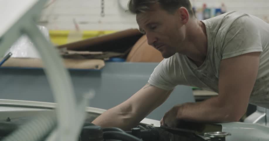 A mechanic looks under the hood of a car checking things