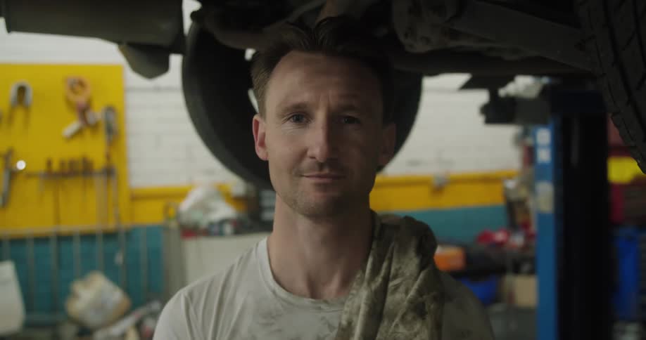 A man standing and staring underneath a vehicle in a garage