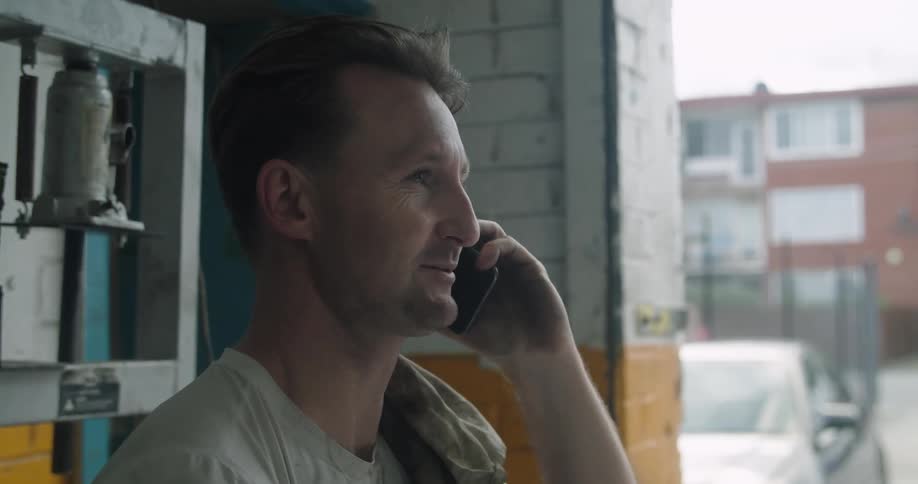 Car mechanic with a dirty white t shirt talks on the smartphone in the garage