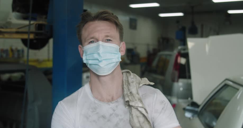 A man with a mask standing in a garage with vehicles in the background