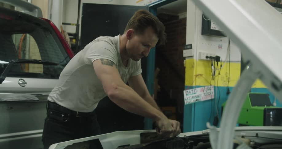 A mechanic tightens something under the hood of a vehicle