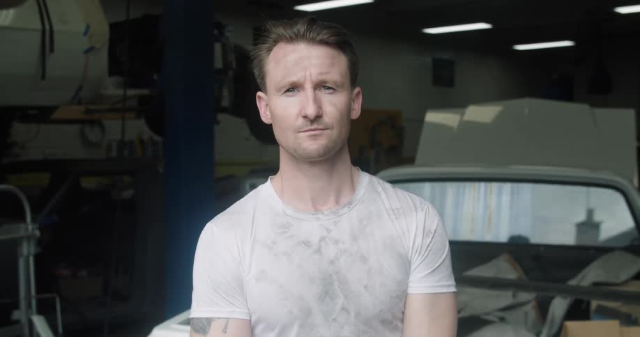 A mechanic standing in a shop in front of a car