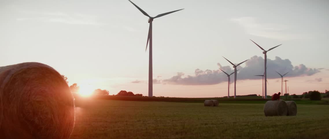 Sun sets behind wind turbines on field with hay bales