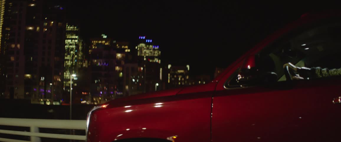 A person drive a large red suv at night near a large metropolitan area