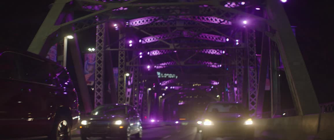 Vehicles travel across a bridge illuminated by purple lights