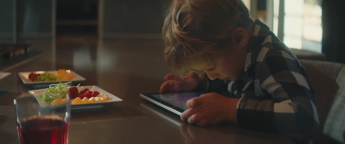 A young boy uses a tablet while sitting at a dining table