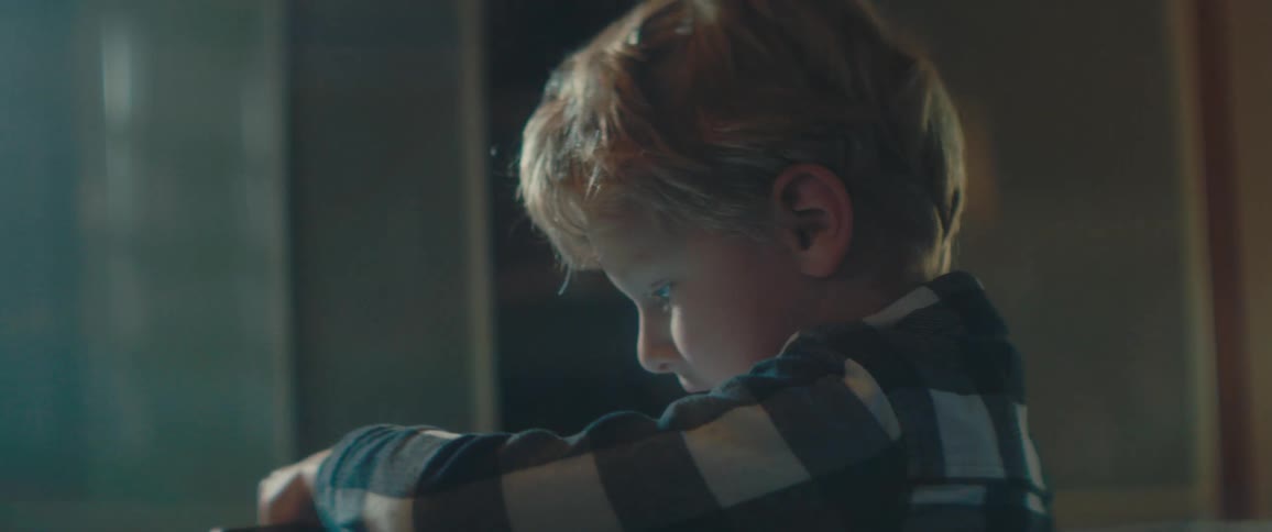 Blonde boy with a plaid shirt sits at a table and uses a tablet