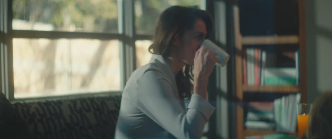 A woman drinks from a coffee mug as she sits at a dining table with a man and child