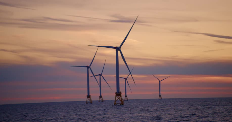 Wind turbines on the ocean spin under the orange evening sky
