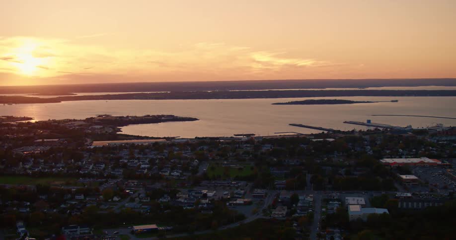 An aerial view of a neighborhood on the coast with the sun setting over the water