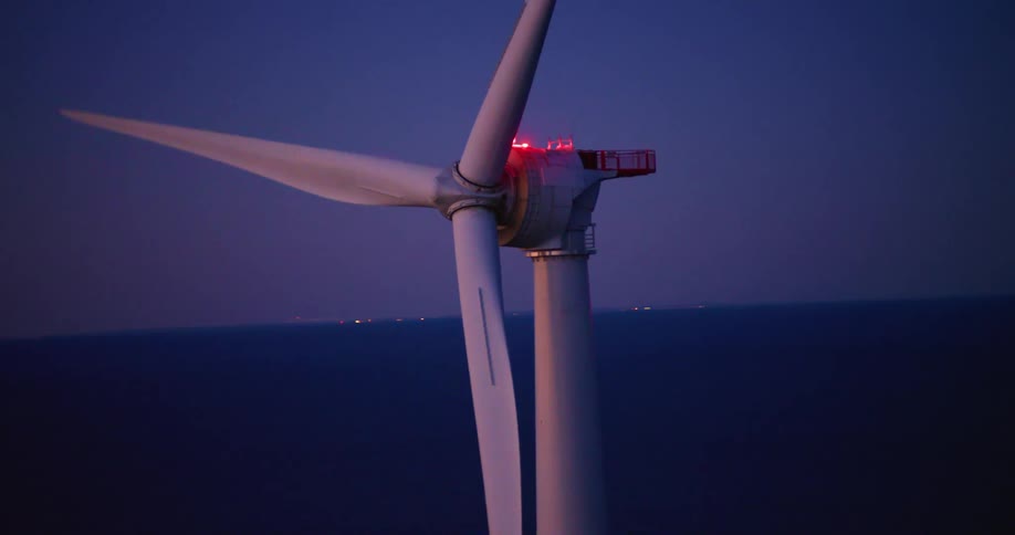 Close aerial view of a wind turbine with blinking red lights spinning at sunset