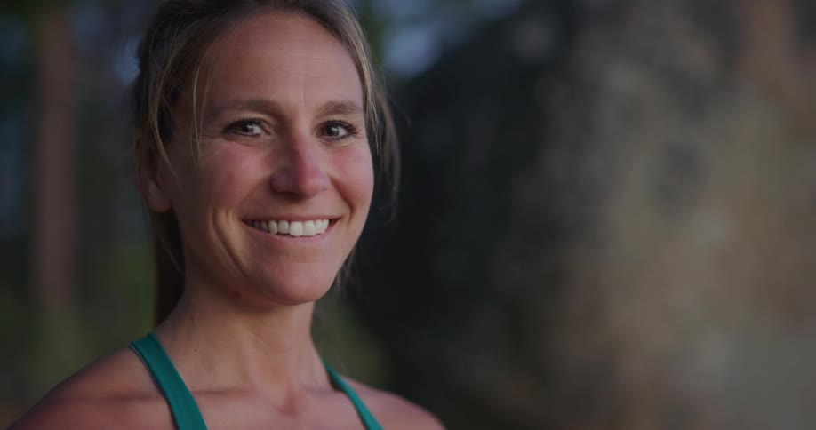A middle aged caucasian turns her head to smile into the camera while standing outdoors during the day