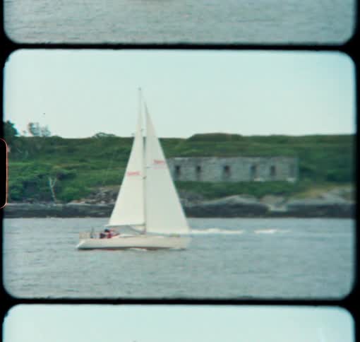 A white sailboat sails along the coast of Maine in the Summer