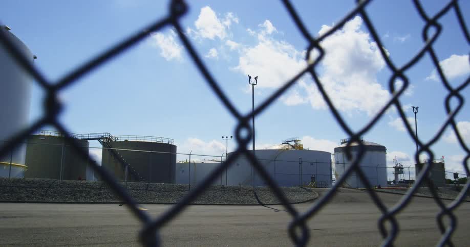 A chain link fence is pulled to the left while an oil field is pulled into focus