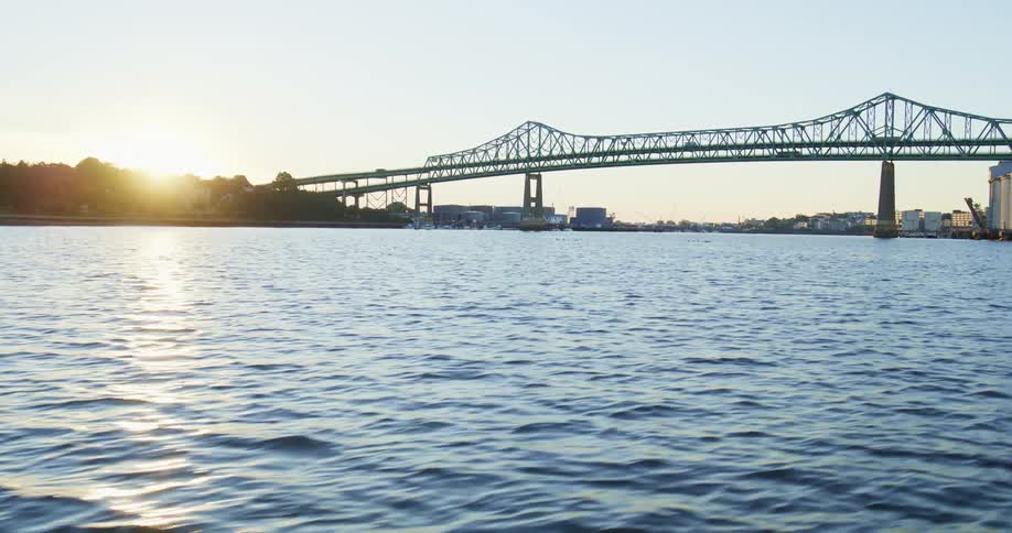 Sun sits at horizon as traffic crosses suspension bridge near town