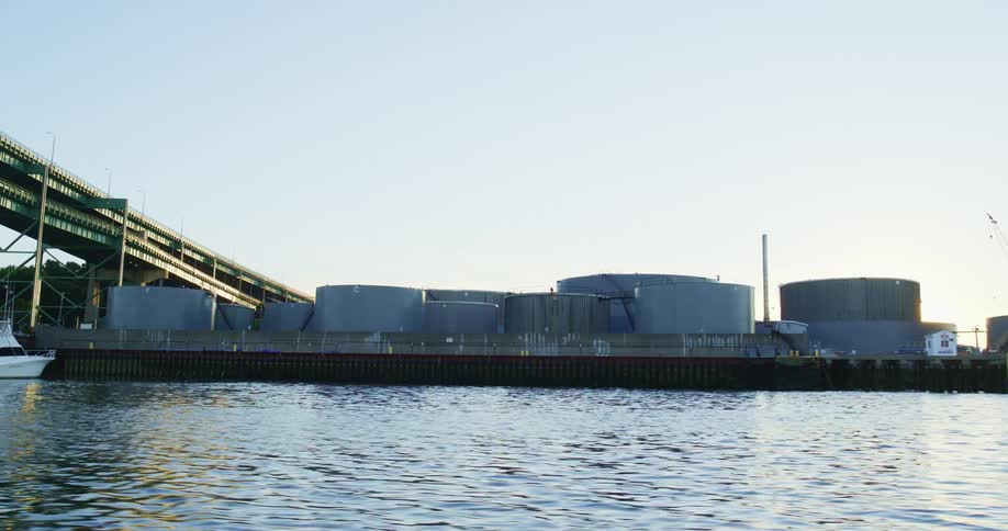 A factory near a coast with water and a boat with the sky in the background
