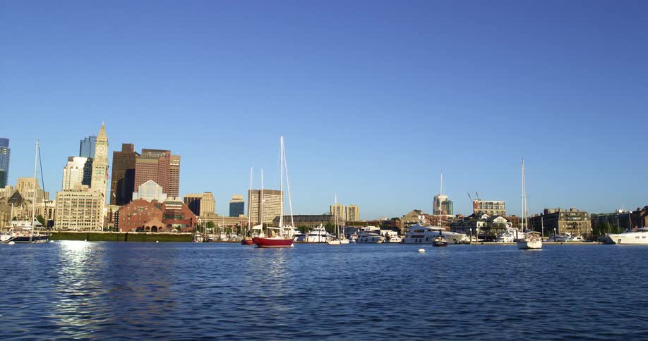 Multiple boats sits in a waterway beside a city