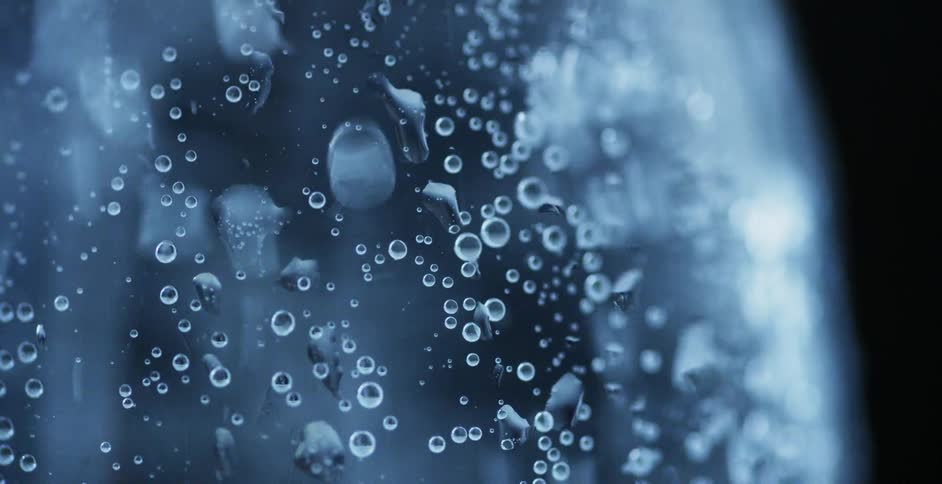 A clear carbonated beverage bubbles to the surface as condensation forms on the glass