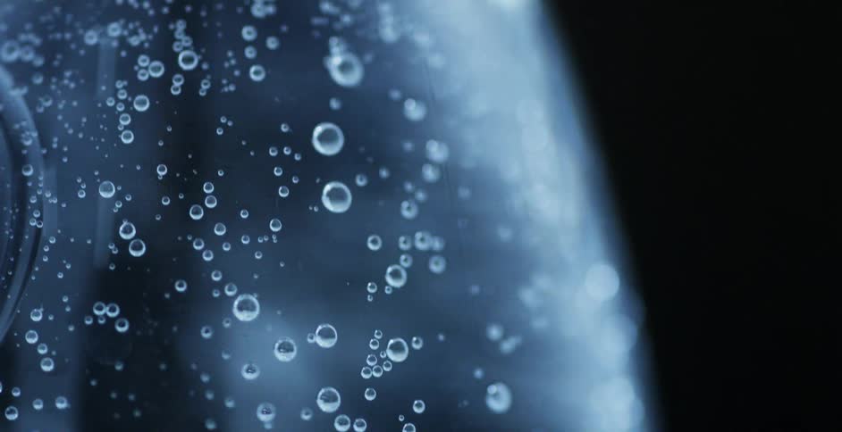 Bubbles rise to top of clear liquid against black background