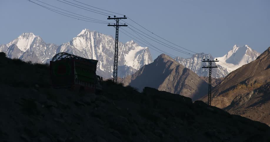 A box truck with a arched cage cover drives down a rural road near a mountain range