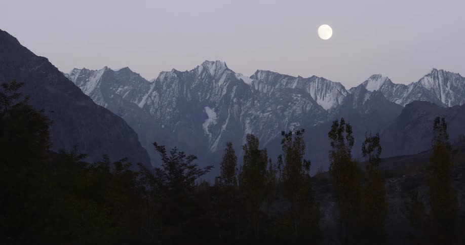 The moon looms over snow capped mountain ridge in the evening