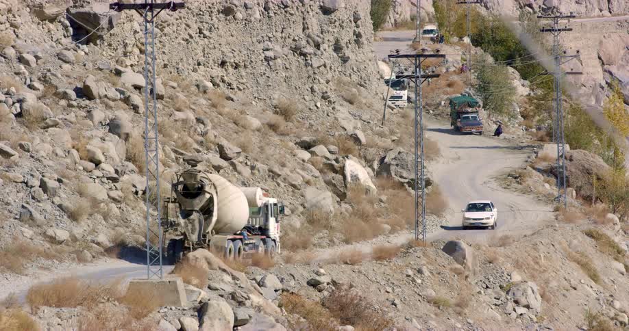 A road on a cliff with utility poles with vehicles and rocks