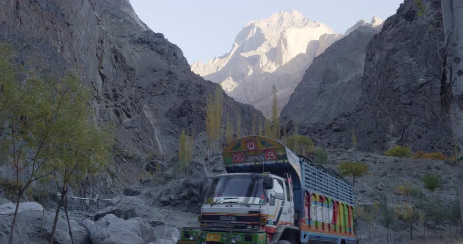A pair of colorfully painted trucks travel through gray stony mountains during the day