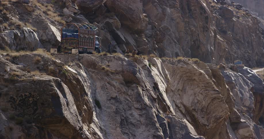 A group of men sit beside a colorful truck on a rocky cliff during the day