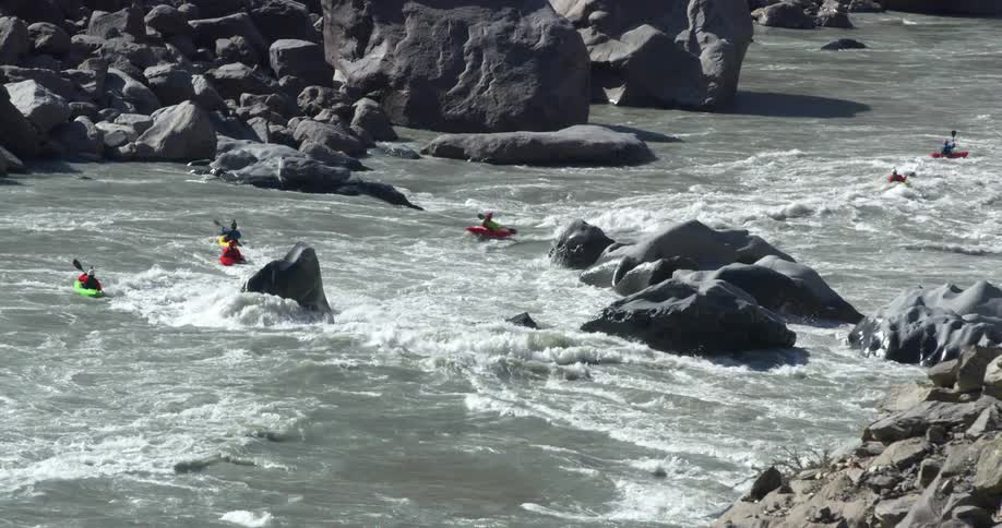 Group of people kayak along river navigating rapids and avoiding boulders