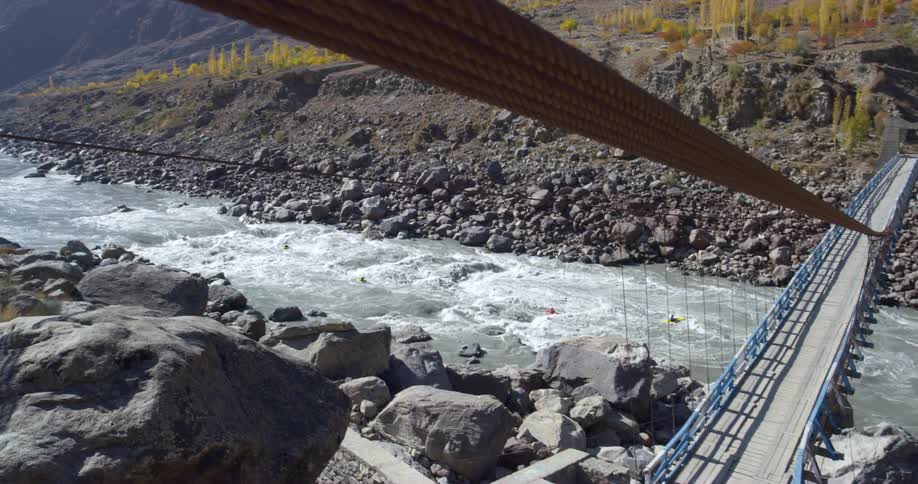 A group of kayakers travel under a bridge on a river during the day