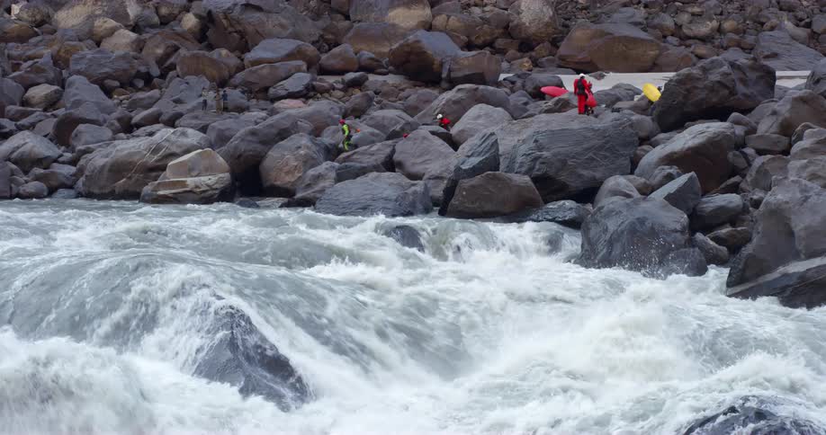 People with canoes walking on rocks next to a river