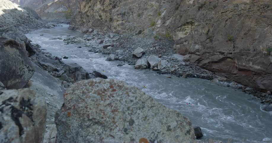 A group of kayakers travel down a river through a canyon on a sunny day