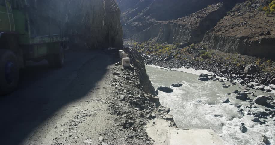 Truck drives on dirt road beside cliff above gorge with river