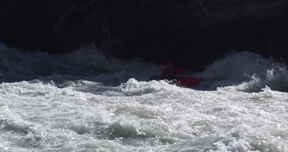 A kayaker attempts to paddle a kayak through the violent waters of a river on a sunny day