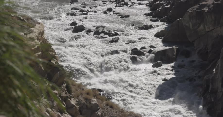A fast rushing rapid filled river is rushing between rocky mountains