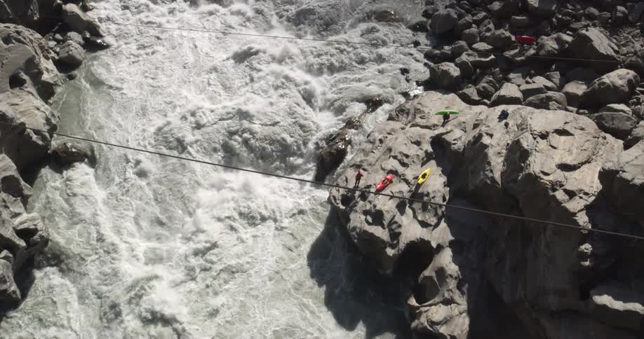 A group of kayakers gather on the stone shore beside a river during the day