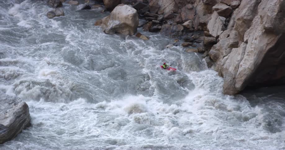 Man on a red kayak paddles in the turbulent waters of a rivers rapids