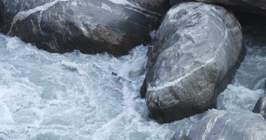 A kayaker drops off a large boulder into swift rapids
