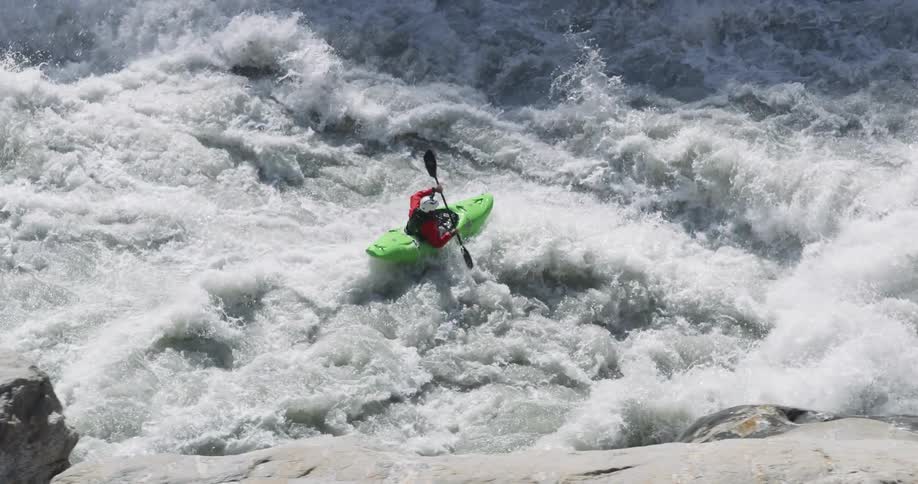 Person paddles kayak down whitewater rapids past stony shore