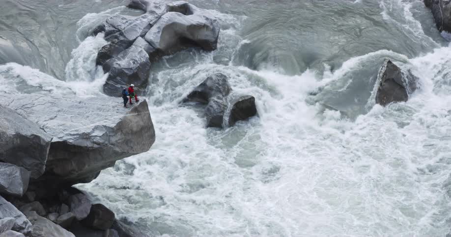 Two men stand on the edge of a promontory over the turbulent waters of a rivers rapid