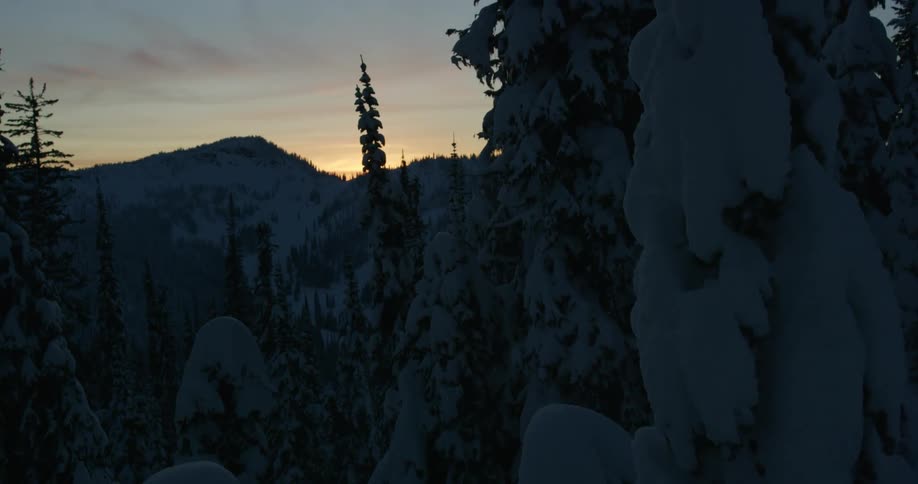 Sun starts to peak over mountain as snow and ice cover mountain and nearby conifer forest